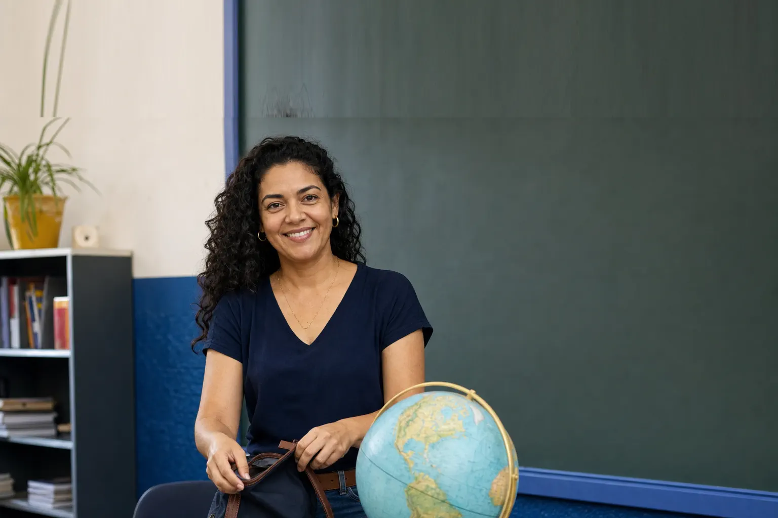 Professora sorridente em sala de aula guardando mochila sobre a mesa, ao lado de globo terrestre escolar